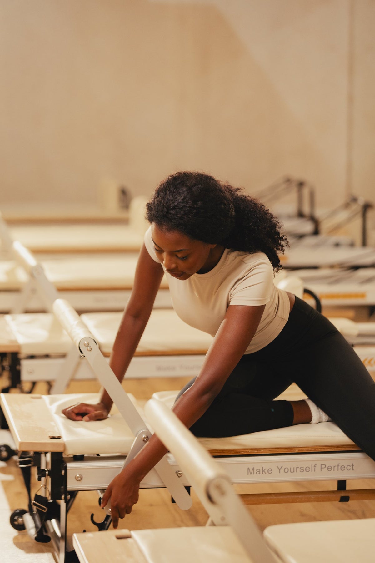 Pilates instructor adjusting a reformer, wearing the VYVRA Layer Tee