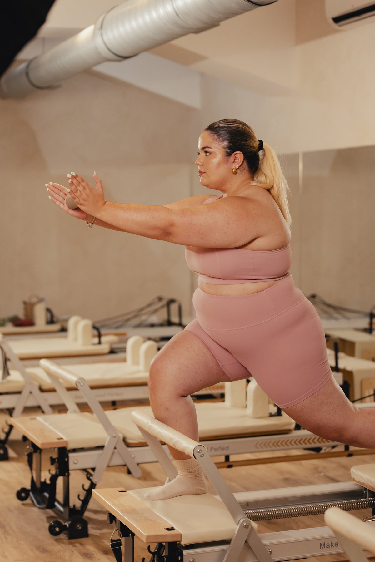 Lunge on the reformer in the VYVRA Edge Bra and Classic Motion Shorts in Soft Blush